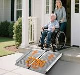 Persona mayor en silla de ruedas usando una rampa portátil de aluminio para salvar el escalón de un portal